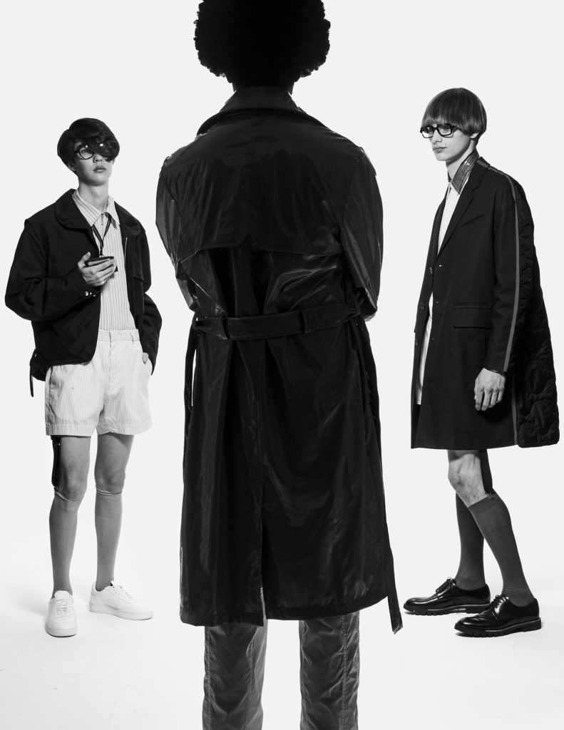 FROM LEFT:  KEVIN WEARS  jacket LANVIN. shirt and shoes SANDRO. shorts No21. glasses RETRO SUPER FUTURE. lanyard PALM ANGELS. socks INTIMISSIMI. ROBBY WEARS  coat RAINS. pants VERSACE. LIAM WEARS  coat, shirt, shorts No21. glasses RETRO SUPER FUTURE. socks INTIMISSIMI. shoes BALLY.