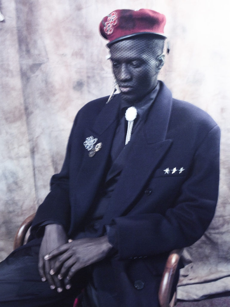 MUSA WEARS hat CUSTOM AUSTIN BLAISDELL. coat, jacket, shirt, pants. tie and brooches (right) RAINBOW UNICORN BIRTHDAY SURPRISE. brooches (left) G. SHERMAN JEWELS.