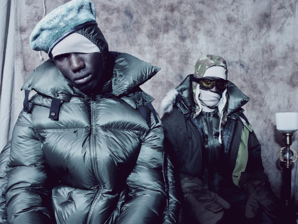 FROM LEFT: MUSA WEARS  hat CHURCH ST SURPLUS. coat MONCLER 5 x CRAIG GREEN. IBBY WEARS  coat N.HOOLYWOOD. coat (underneath) and pants MONCLER 5 x CRAIG GREEN. hood FRONT GENERAL. goggles CHURCH ST SURPLUS. gloves stylist's own.